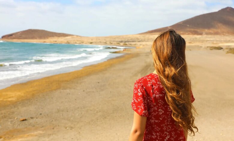 Uma mulher de costas vestida de vermelho em uma praia de Tenerife