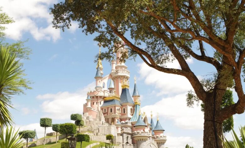 O castelo da Disneyland Paris cheio de pequenas torres e próximo a diversas árvores