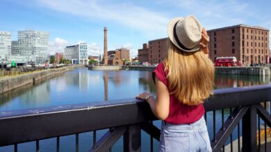 Uma turista, de costas para o corrimão de uma ponte, contemplando o horizonte de Liverpool