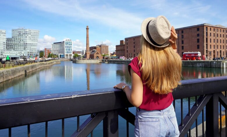 Uma turista, de costas para o corrimão de uma ponte, contemplando o horizonte de Liverpool